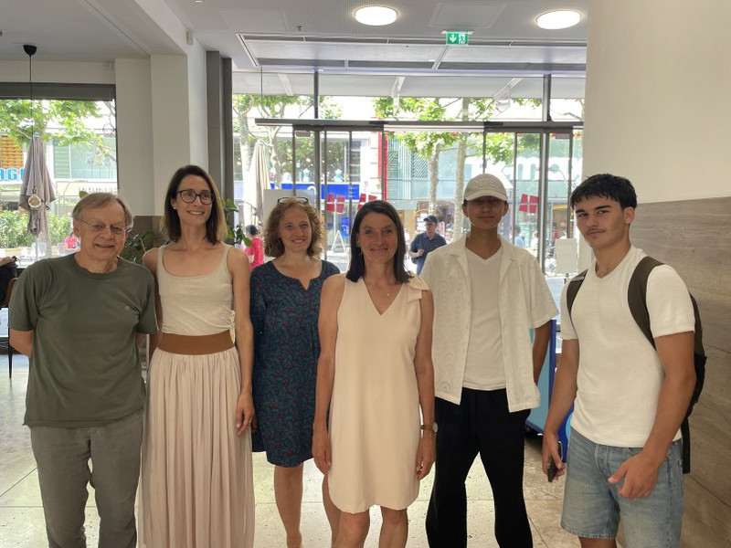 Nematullah Rajabi und Fabiano Kolaj aus dem AVdual 2, ansonsten Sibylle Schorpp, Christine Kegreiß, Nadja Großmann und Walle Sayer (v.r.n.l.) Gruppenfoto in einem hellen Foyer: Dichter Walle Sayer, Schulsozialarbeiterin Nadja Großmann, zwei Lehrerinnen und zwei Schüler stehen lächelnd vor großen Glasfronten; im Hintergrund Fußgängerzone mit Bäumen.
