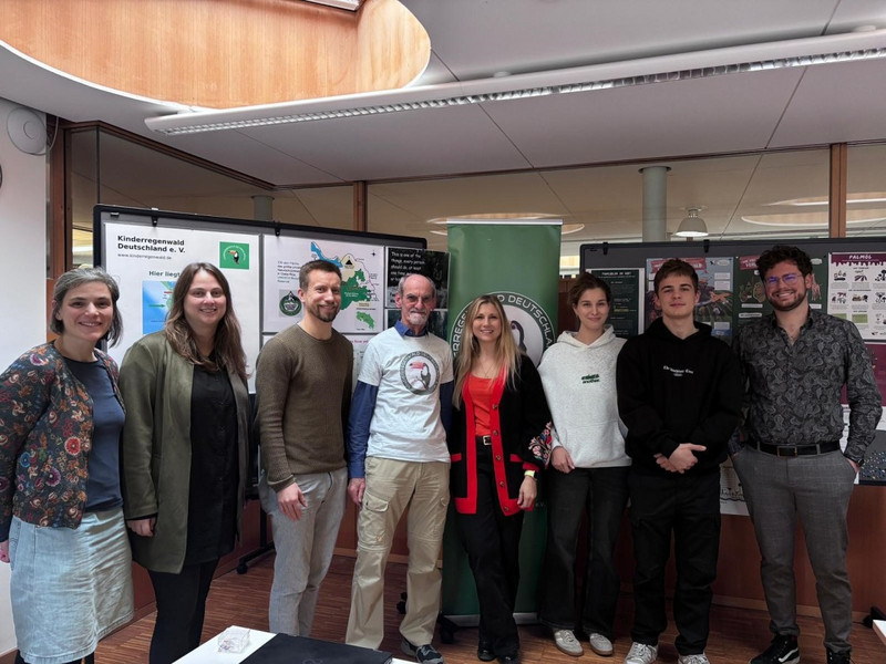 Gruppenfoto vor Infostellwänden zum Regenwaldprojekt. In der Mitte Roland Paul vom Kinderregenwaldprojekt und Melanie Hörz mit Schülersprecher*innen und Kolleg*innen der Hilde-Domin-Schule
