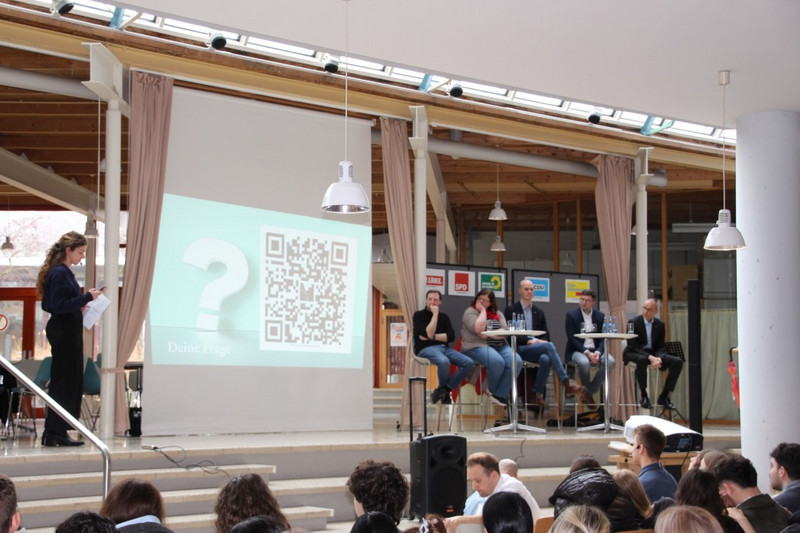 Schülersprecherin Svenja Ensinger (links) richtet die via Menti-App erhobenen Publikumsfragen an die Kandidierenden