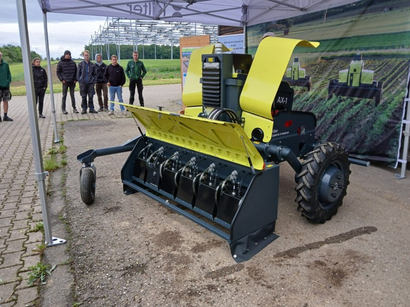 Station 4: Robotics: Applikationstechnik Vorführstand: Gelb-schwarzer Feldroboter mit geöffnetem Mulch-/Hackwerk, große Reifen; daneben beobachten Schülerinnen und Schüler die Technik unter einem Pavillon am Feldrand.