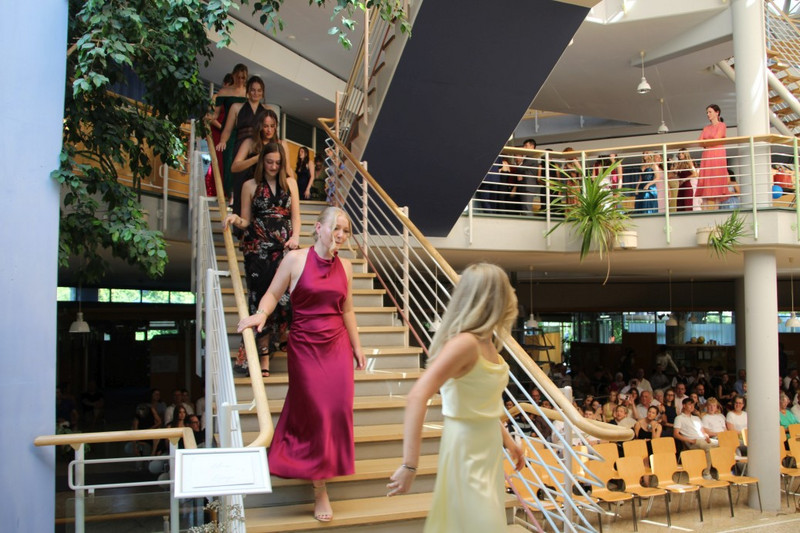 biball im Schulfoyer: Schülerinnen und Schüler in Abendkleidung steigen die Treppe hinab; Gäste verfolgen den Einzug von den Sitzreihen und der Galerie.