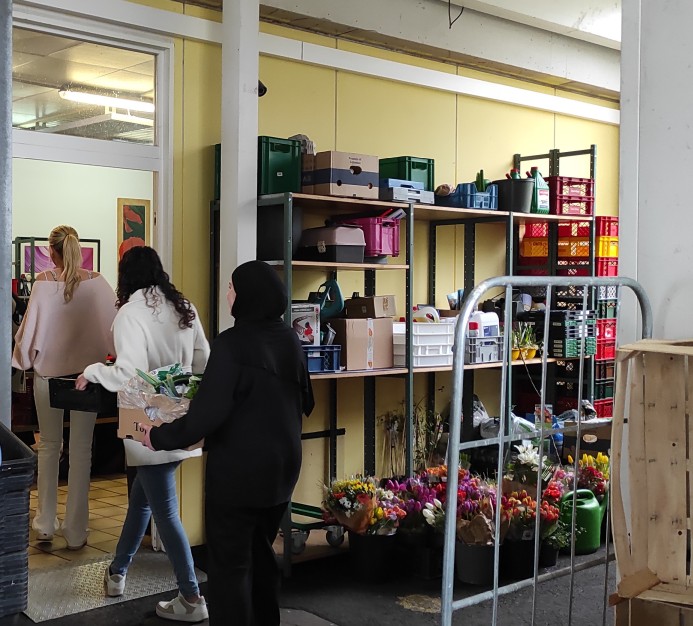 drei Schülerinnen der Klasse 1BKSP1 im linken Bildrand gehen durch einen Lagerraum des Tafelladens